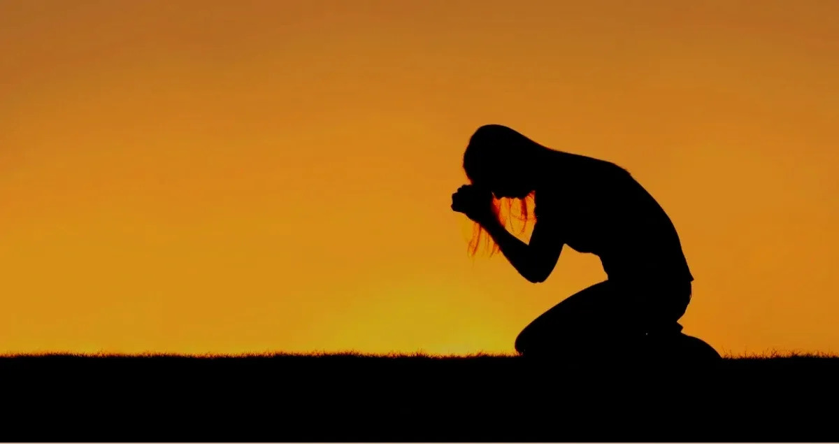 A person kneeling in prayer at sunset